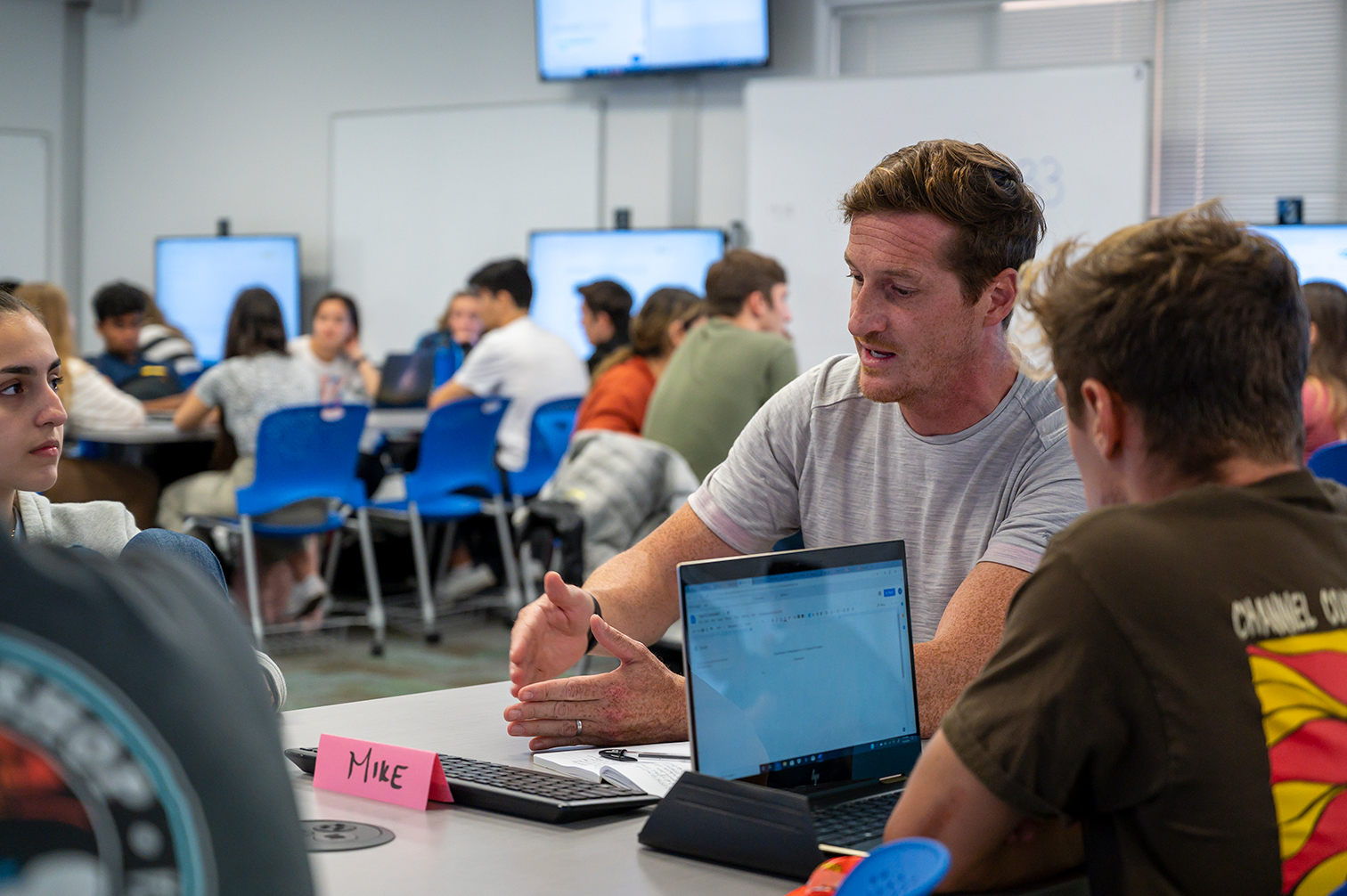 instructor seated at table with two people and one laptop