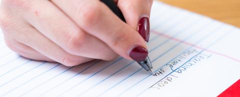 hand with a pen writing on a pad of paper
