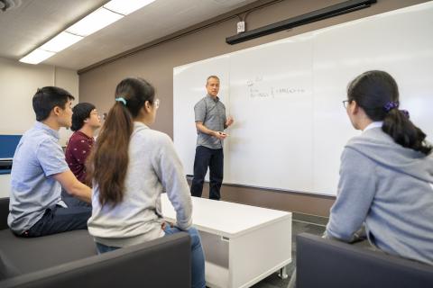 person standing at whiteboard in front of four seated students